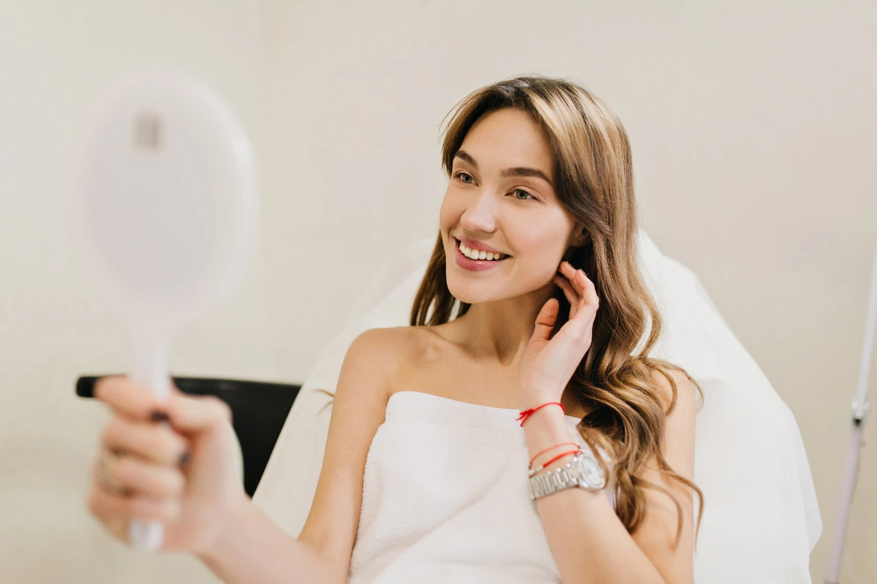 Unlock Timeless Beauty with Botox: The Secret to Youthful Skin 2 Happy beautiful woman with long brunette hair after cosmetology therapy smiling to mirror in white r